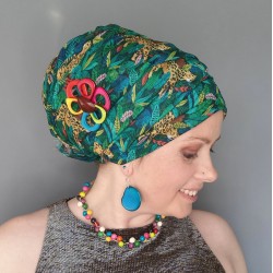 Model with her head turned to one side, wearing a multi green headscarf with yellow cheetahs on it and colourful jewellery.